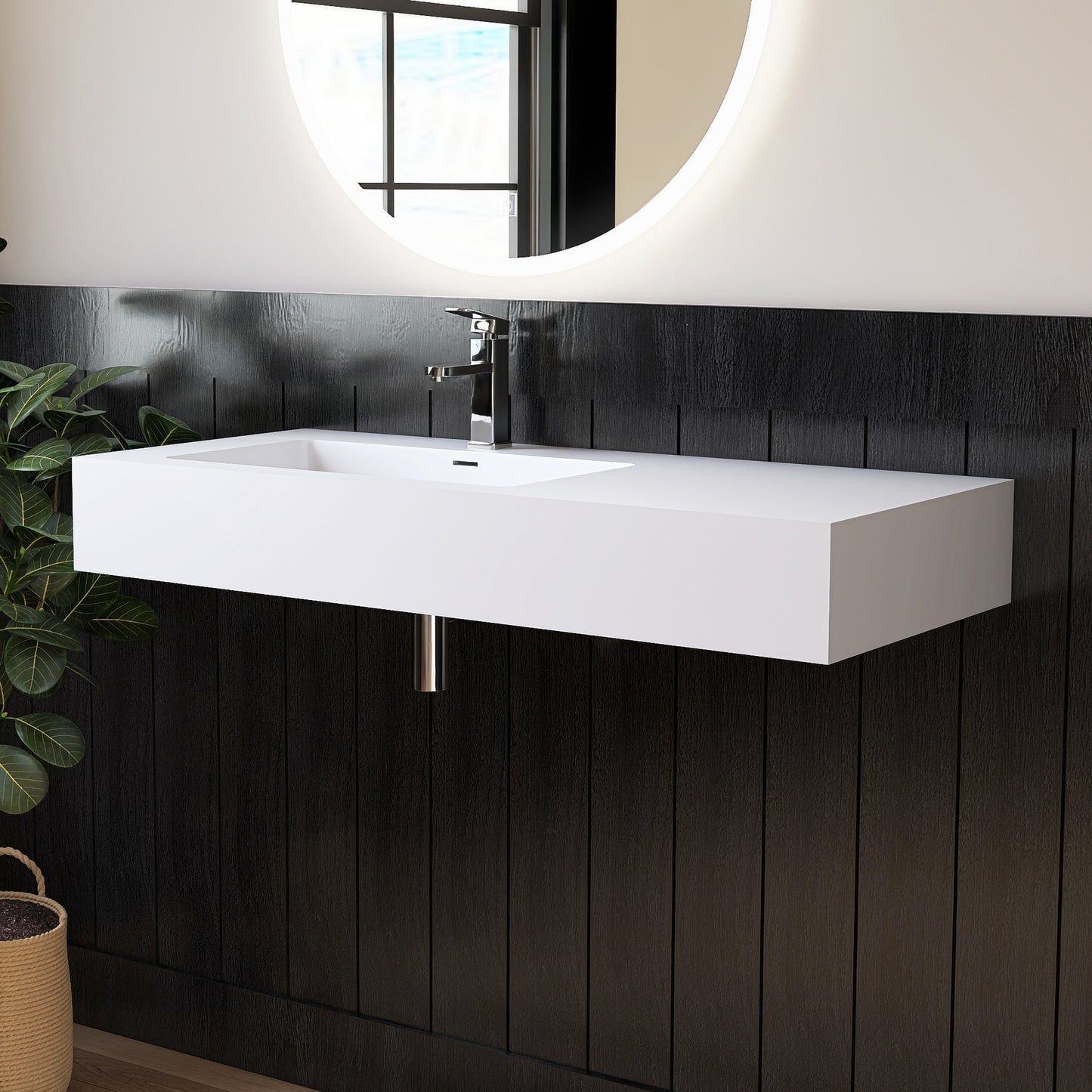 White wall-mounted sink in a bathroom with black tiled walls and a round mirror.