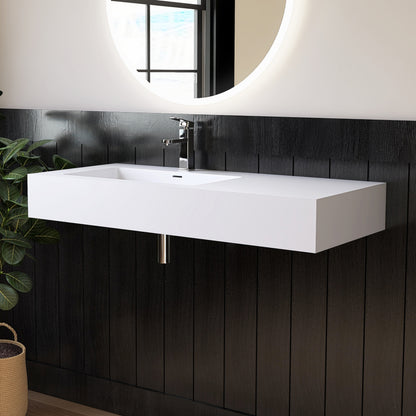 White wall-mounted sink in a bathroom with black tiled walls and a round mirror.