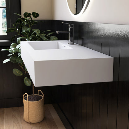 Modern bathroom with a white wall mounted sink, black tiled wall, and a plant.