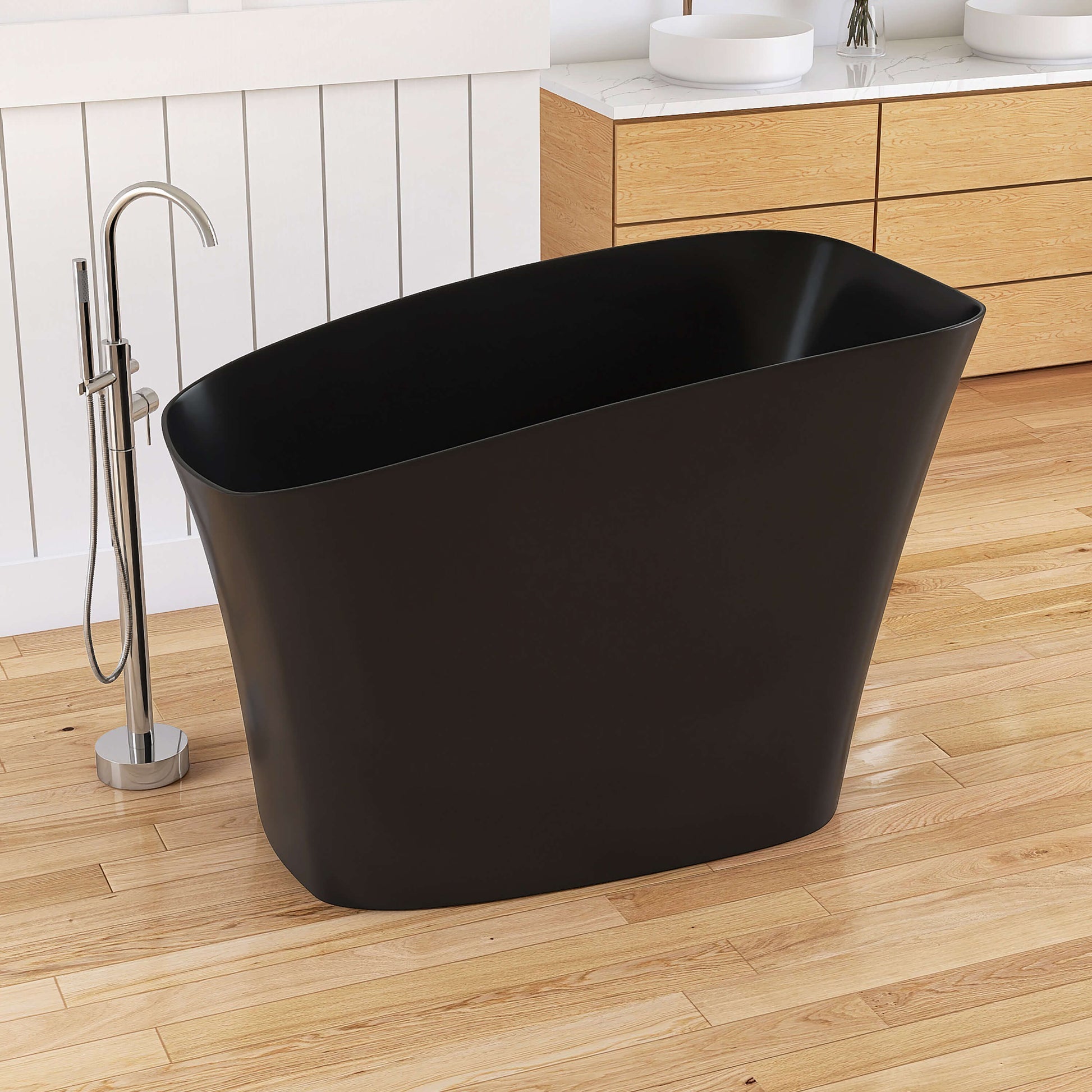 Black freestanding bathtub in a modern bathroom with wooden floor and white walls.