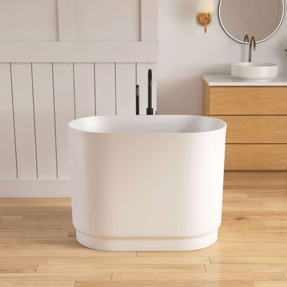 White freestanding bathtub in a modern bathroom with wooden flooring and cabinetry.