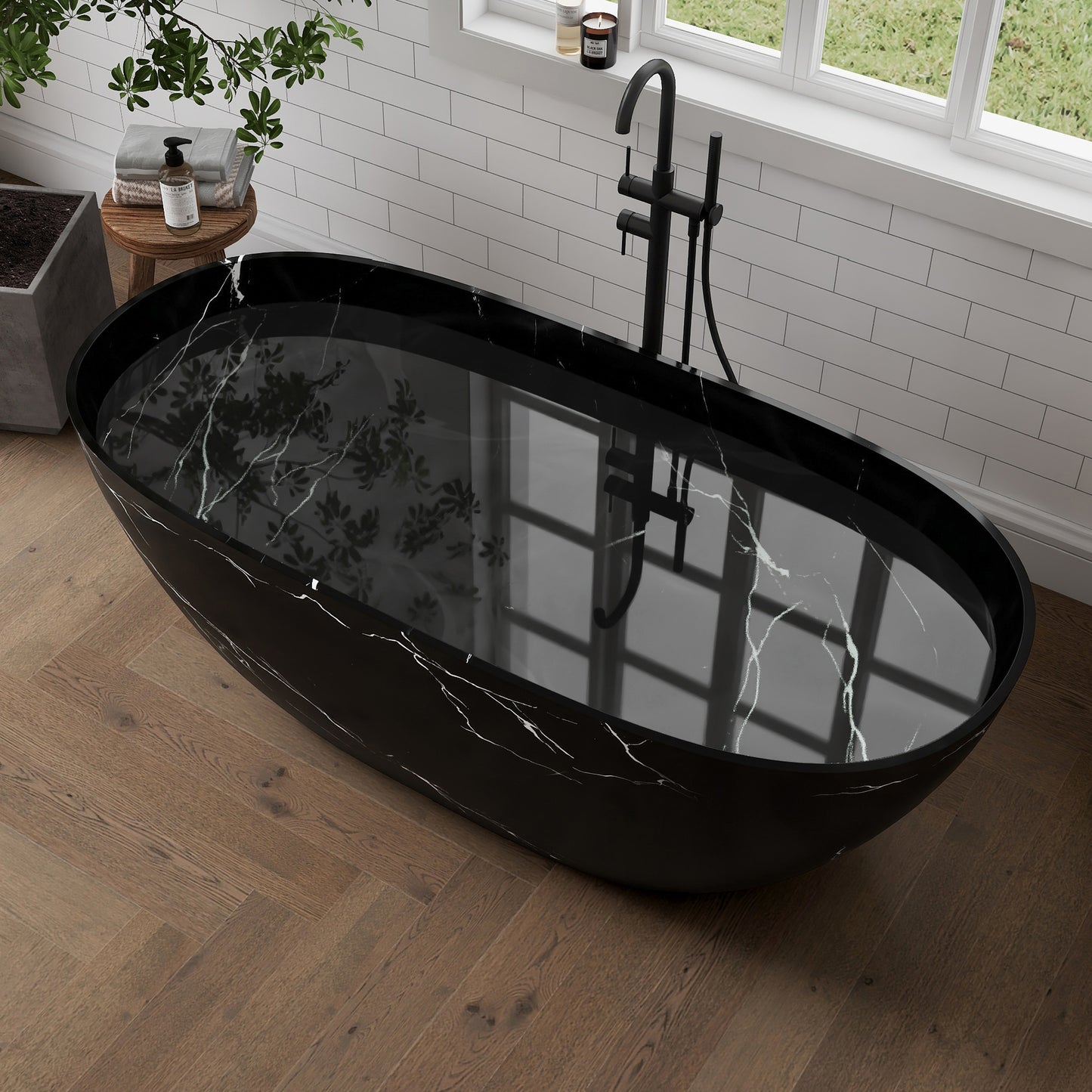 Black marble-pattern freestanding bathtub in a modern bathroom with wooden floor and window.