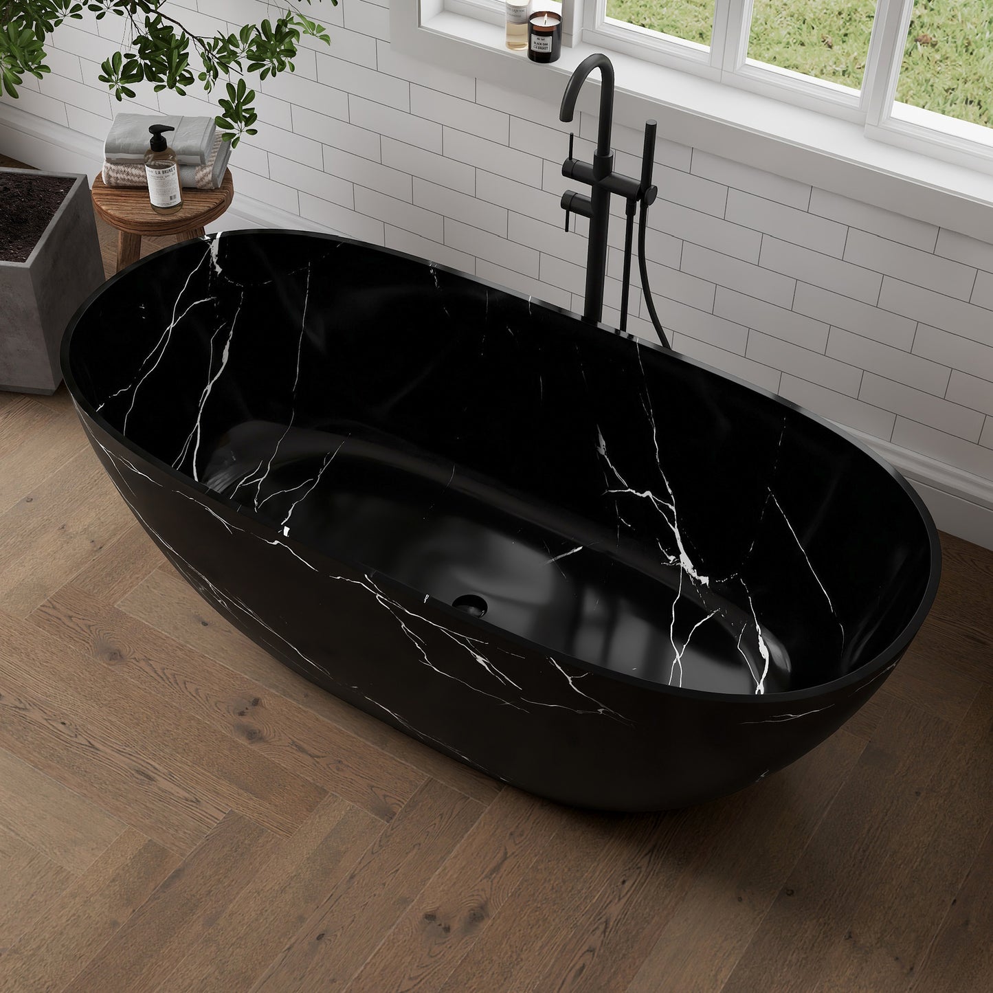 Black marble-patterned freestanding bathtub in a modern bathroom with a window and plant.